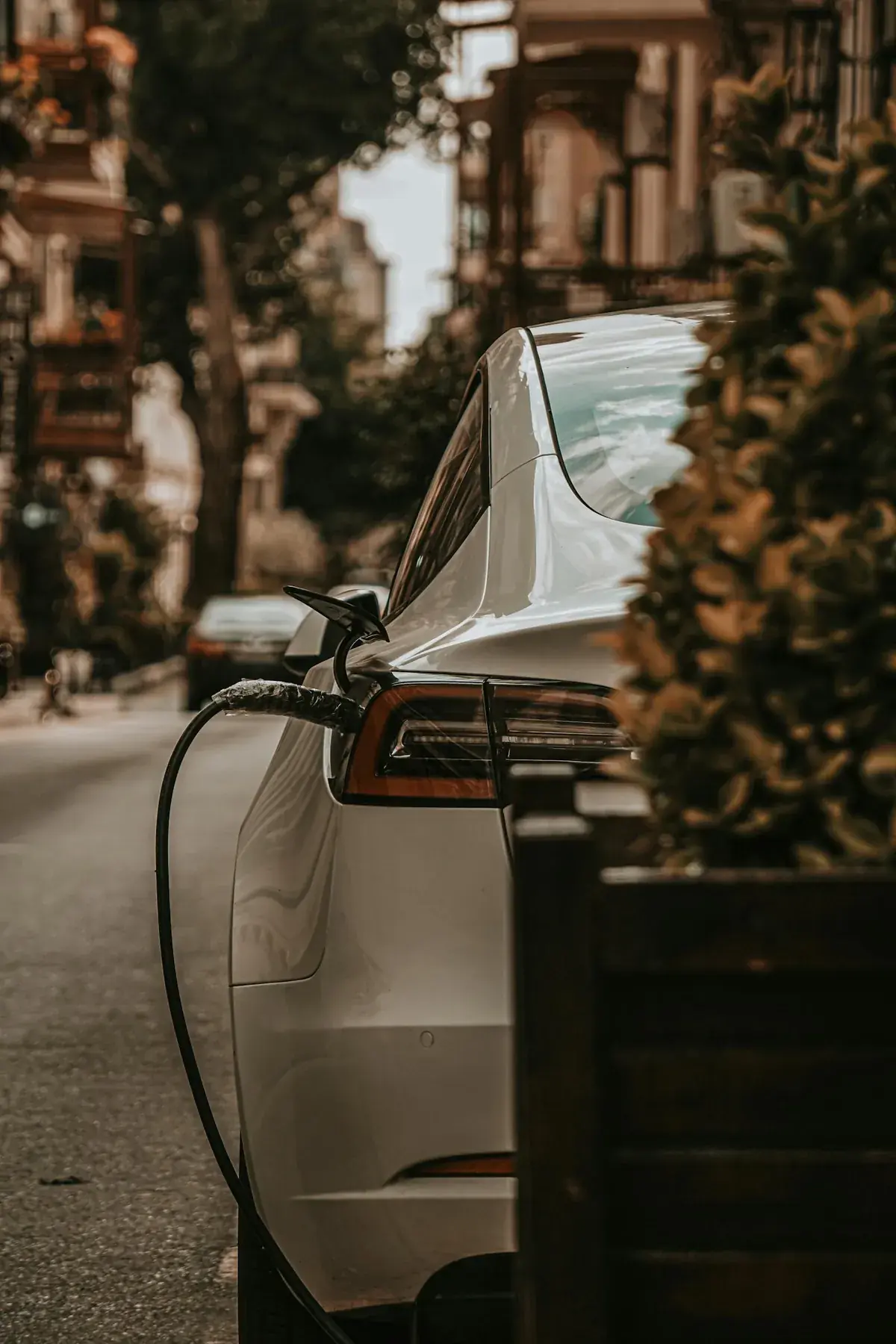 Voiture électrique en cours de recharge sur une borne publique en ville, comparatif électrique vs hybride 2026